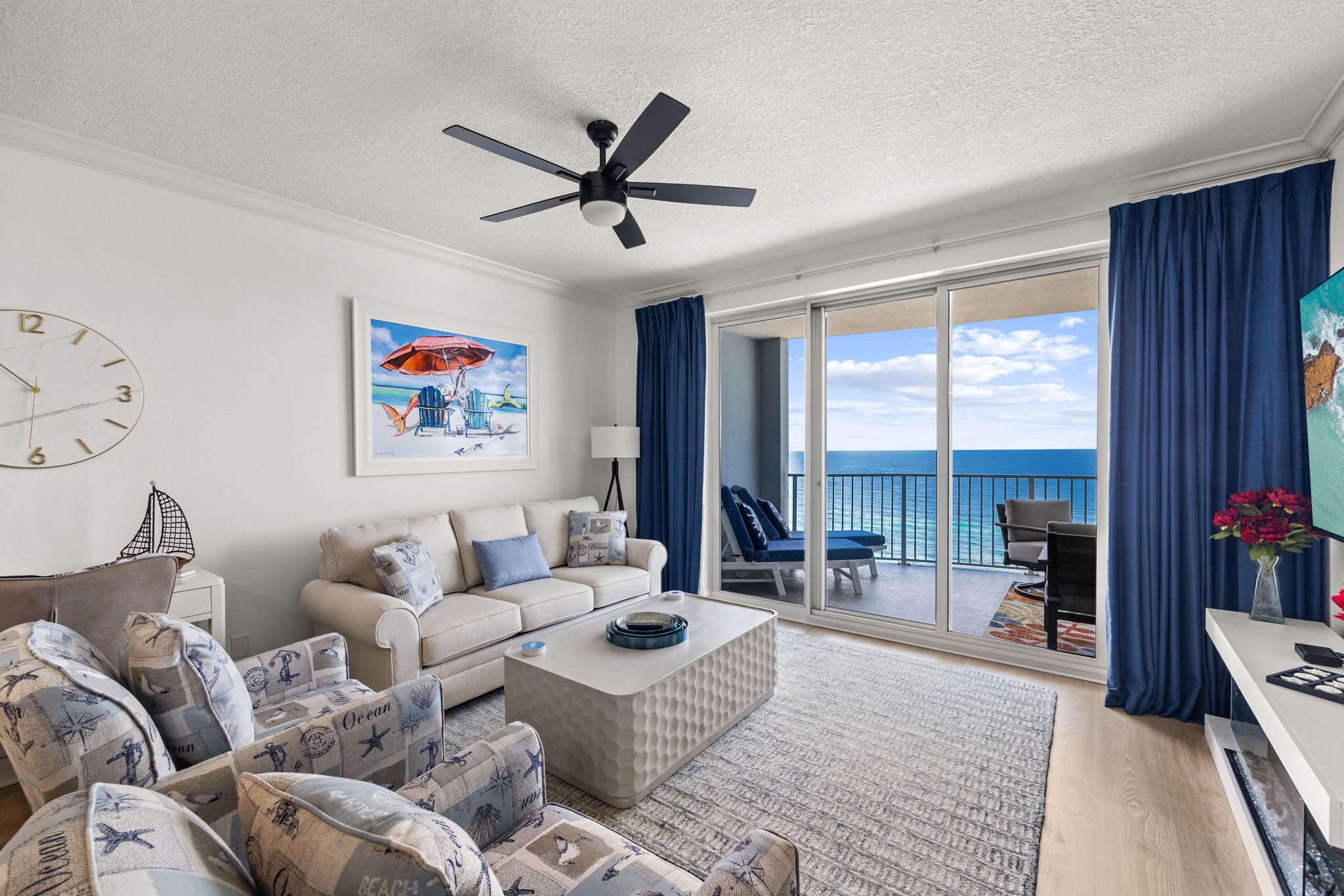 A spacious living room with a large window, a ceiling fan, and a view of the ocean.