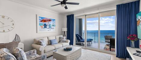 A spacious living room with a large window, a ceiling fan, and a view of the ocean.
