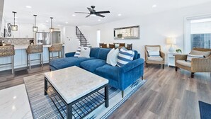 Ein modernes Wohnzimmer mit einem blauen Modulsessel, einem Couchtisch, Korbstühlen und einem Deckenventilator.