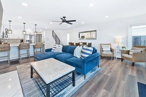 Ein modernes Wohnzimmer mit einem blauen Modulsessel, einem Couchtisch, Korbstühlen und einem Deckenventilator.