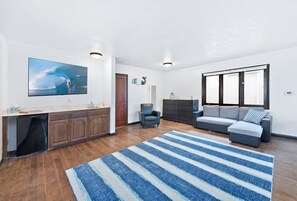 A modern living room with a large flat-screen TV, a grey sofa, a blue-striped rug, and a wooden cabinet. - Stunning Sunset Views,Great for Families W Parking! (Newport Beach)