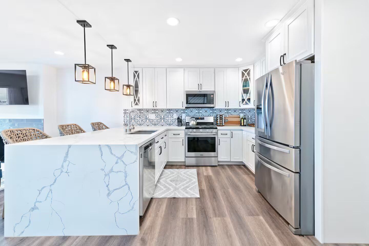 A modern kitchen with white cabinets, a marble island, stainless steel appliances, and pendant lighting.