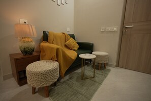 En stue med en grøn sofa, et lille rundt bord, en lampe og en makramé skammel.