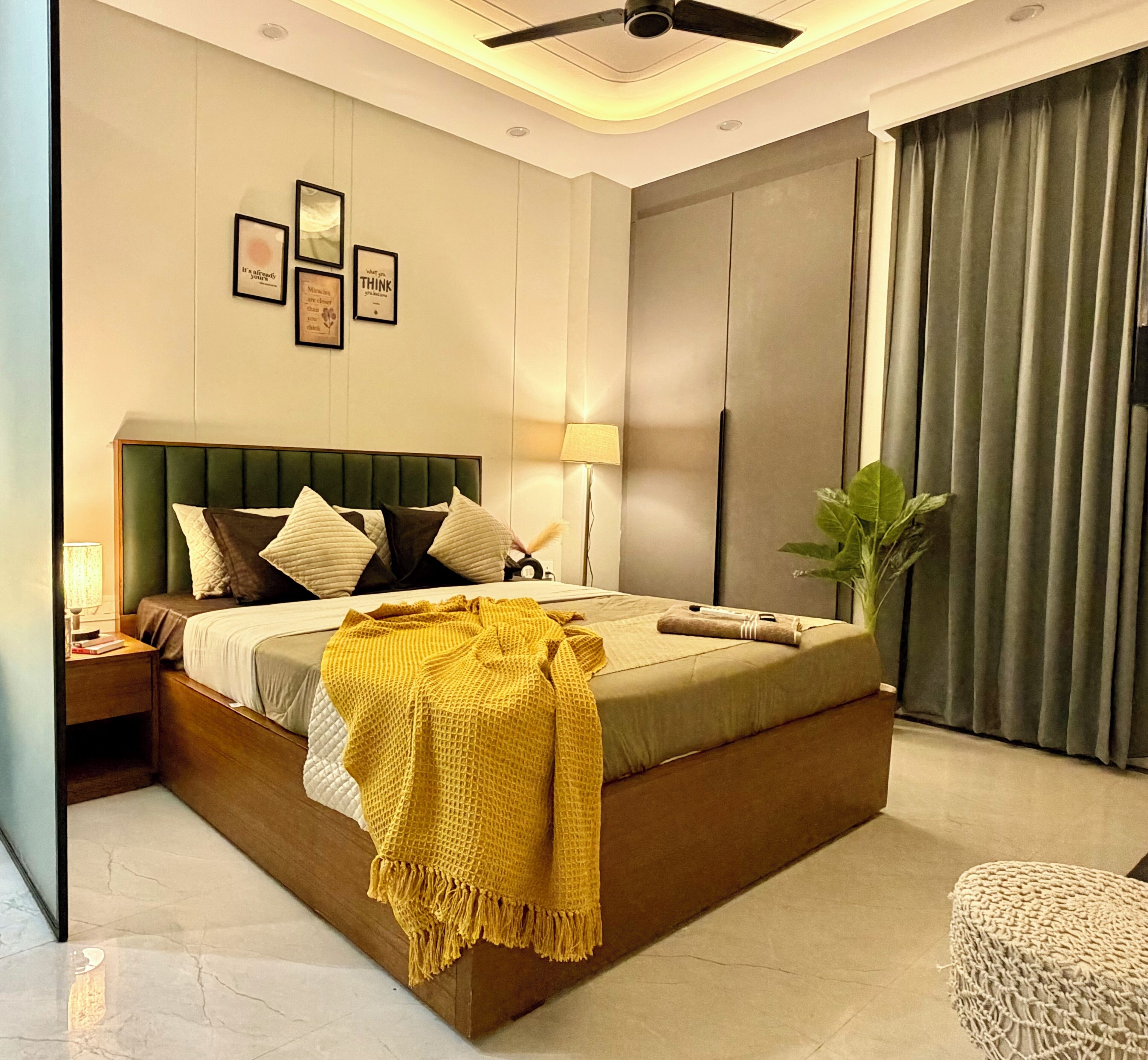 A modern bedroom with a bed, bedside tables, a lamp, a ceiling fan, and a large window with curtains.