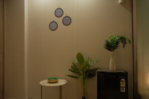 A room with a beige wall, a small round table with a bowl, a potted plant, and a black appliance with a label. - Cozy 1-bedroom apartment on golf course roadGurugram near Metro (Gurugram)