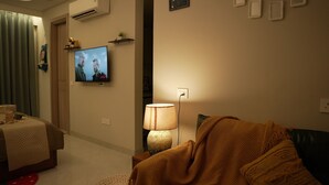 Een woonkamer met een televisie, een lamp en een bank.