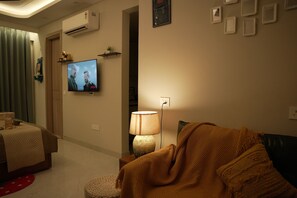 A living room with a television, a lamp, and a sofa. - Cozy 1-bedroom apartment on golf course roadGurugram near Metro (Gurugram)