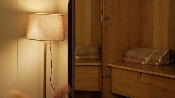 Een kamer met een houten garderobe, een nachtkastje met een lamp en een kapstok.