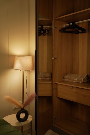 A room with a wooden wardrobe, a bedside table with a lamp, and a hanging coat rack. - Cozy 1-bedroom apartment on golf course roadGurugram near Metro (Gurugram)