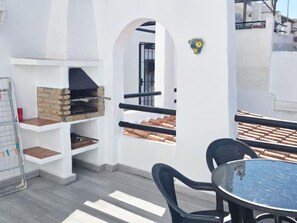 A rooftop terrace with a brick barbecue, outdoor seating, and a view of the cityscape. - Lovely 1-Bedroom Apartment, Pueblo Evita (Benalmádena)