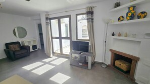 A living room with a sofa, TV stand, fireplace, and large windows. - Lovely 1-Bedroom Apartment, Pueblo Evita (Benalmádena)