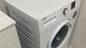 A front view of a white beko washing machine in a bathroom with tiled walls and a white toilet. - Lovely 1-Bedroom Apartment, Pueblo Evita (Benalmádena)