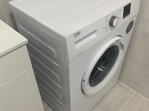 A front view of a white beko washing machine in a bathroom with tiled walls and a white toilet. - Lovely 1-Bedroom Apartment, Pueblo Evita (Benalmádena)