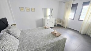Un dormitori amb un llit, un armari, una cadira i una finestra amb cortines.