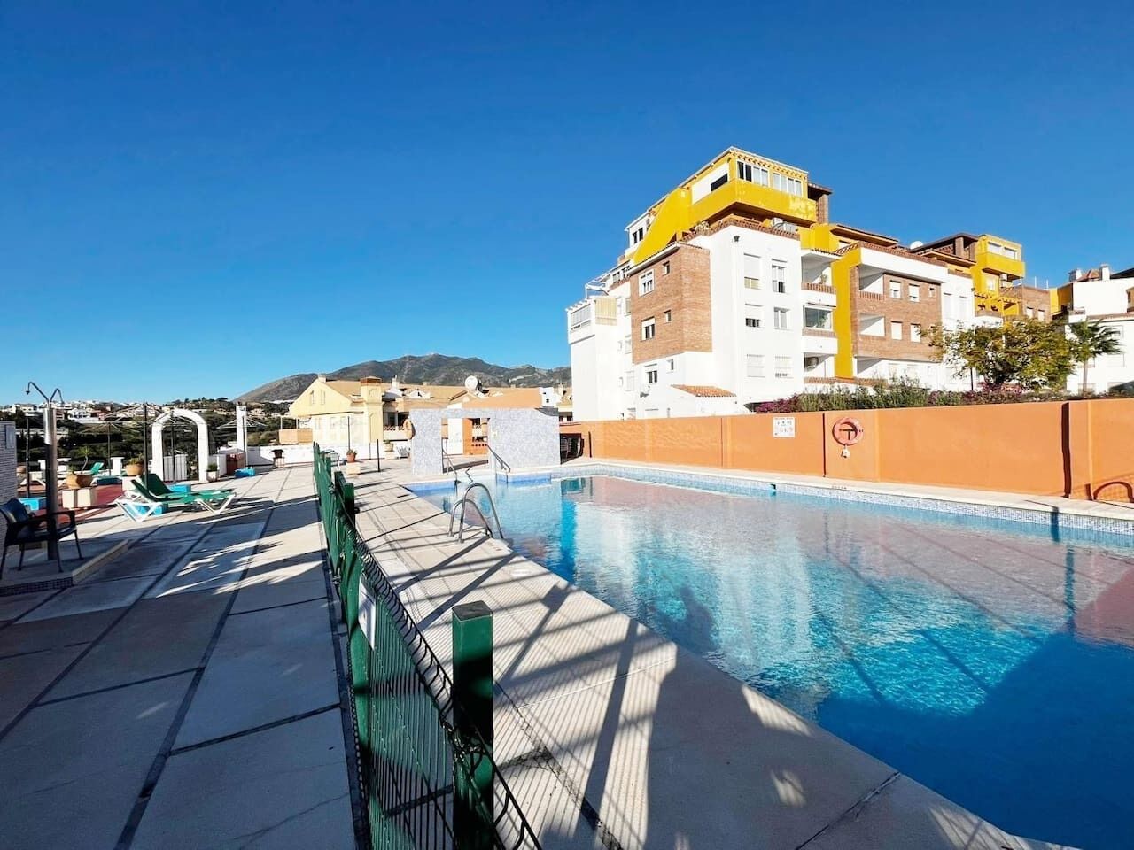 A swimming pool with a sunshade, lounge chairs, and a view of a mountain range.