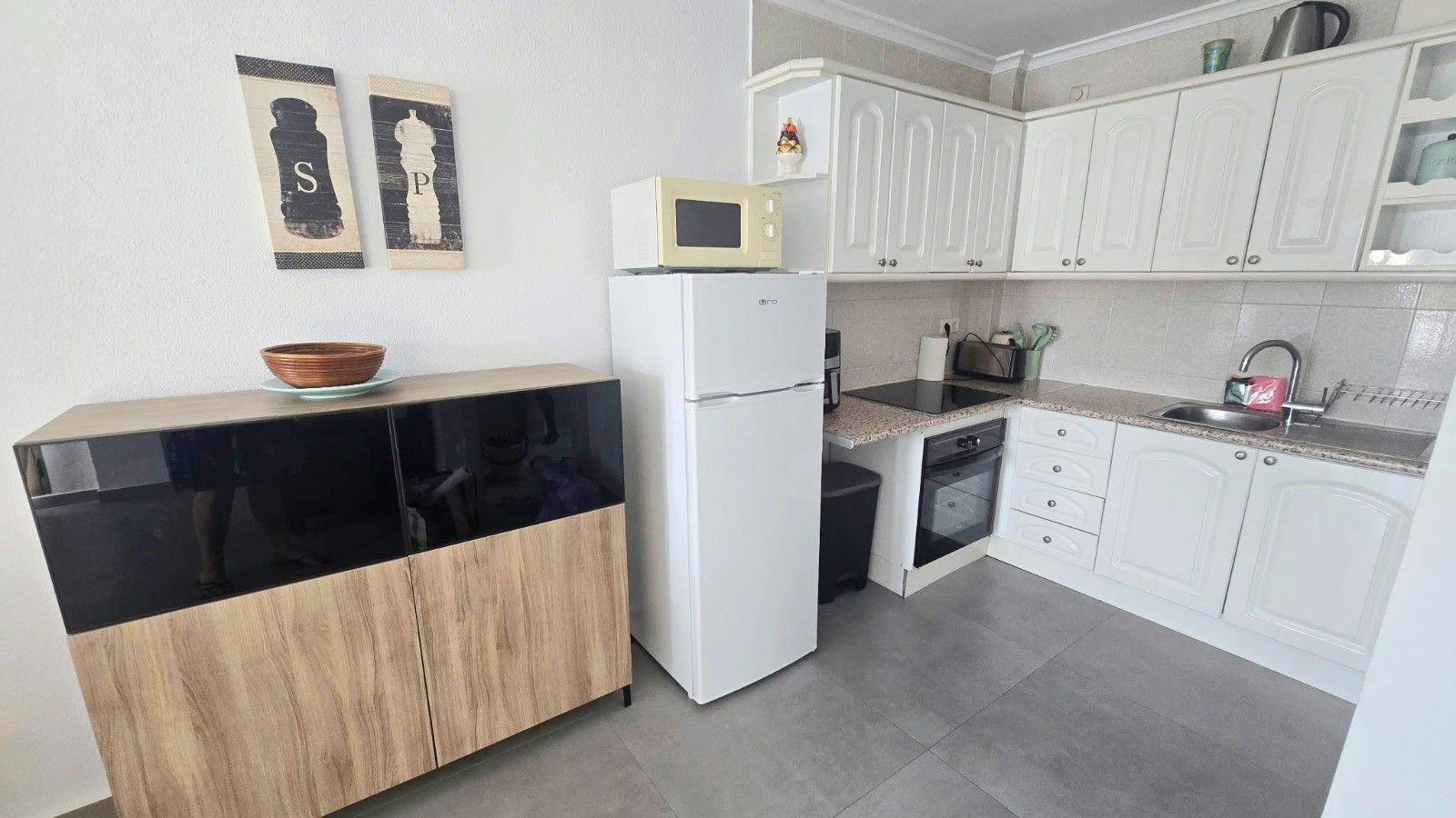 A compact kitchen with white cabinets, a black countertop, a microwave, and a refrigerator.