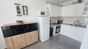 A compact kitchen with white cabinets, a black countertop, a microwave, and a refrigerator. - Lovely 1-Bedroom Apartment, Pueblo Evita (Benalmádena)