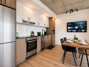 A modern kitchen with stainless steel appliances, wooden cabinets, and a dining area with a table set for four. - Indoor Spa | Gym | 9th Floor | Urban Oasis (Québec)