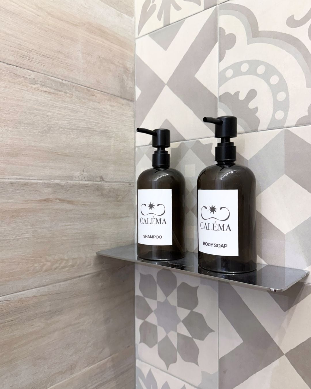 Zwei Flaschen Caléma Shampoo und Duschseife stehen auf einem Regal vor einer Wand mit Muster.