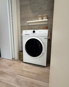 Una lavadora de carga frontal en un cuarto de lavado con piso de madera y un estante arriba.