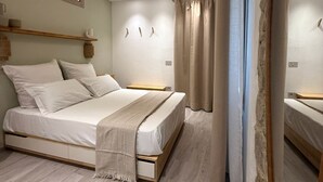A bedroom with a bed, wooden flooring, a ceiling light, and a mirror.