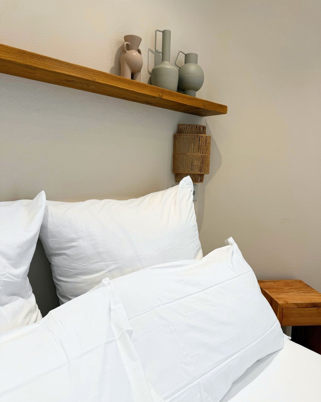 A bed with white bedding, a wooden headboard, and a shelf with decorative vases.