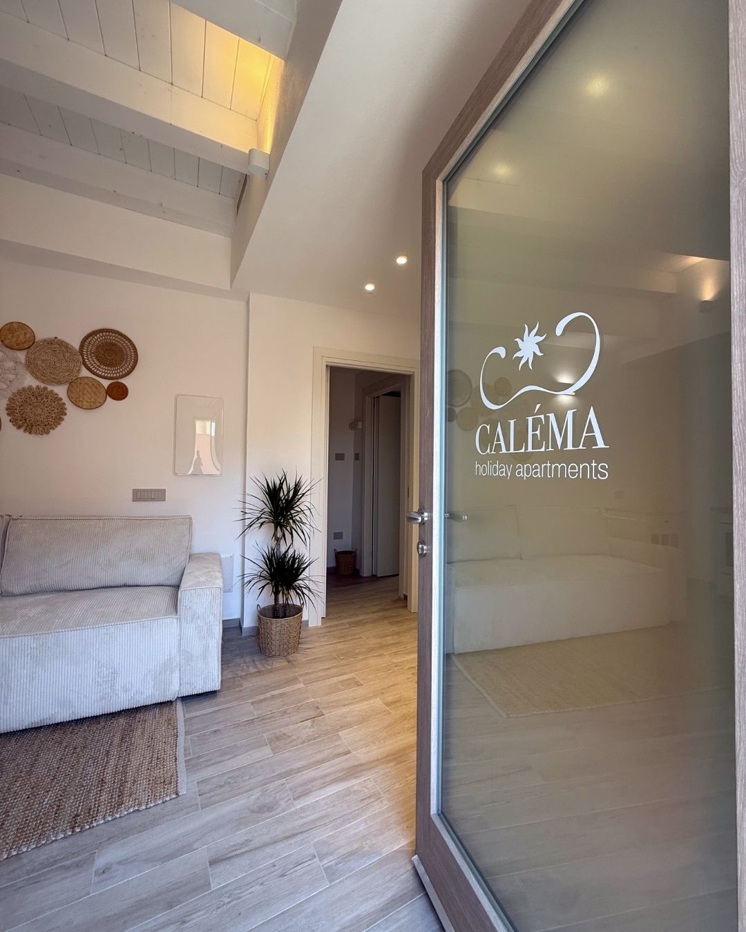 Uma sala de estar moderna com um sofá, plantas em vasos e uma porta de vidro com um logotipo.