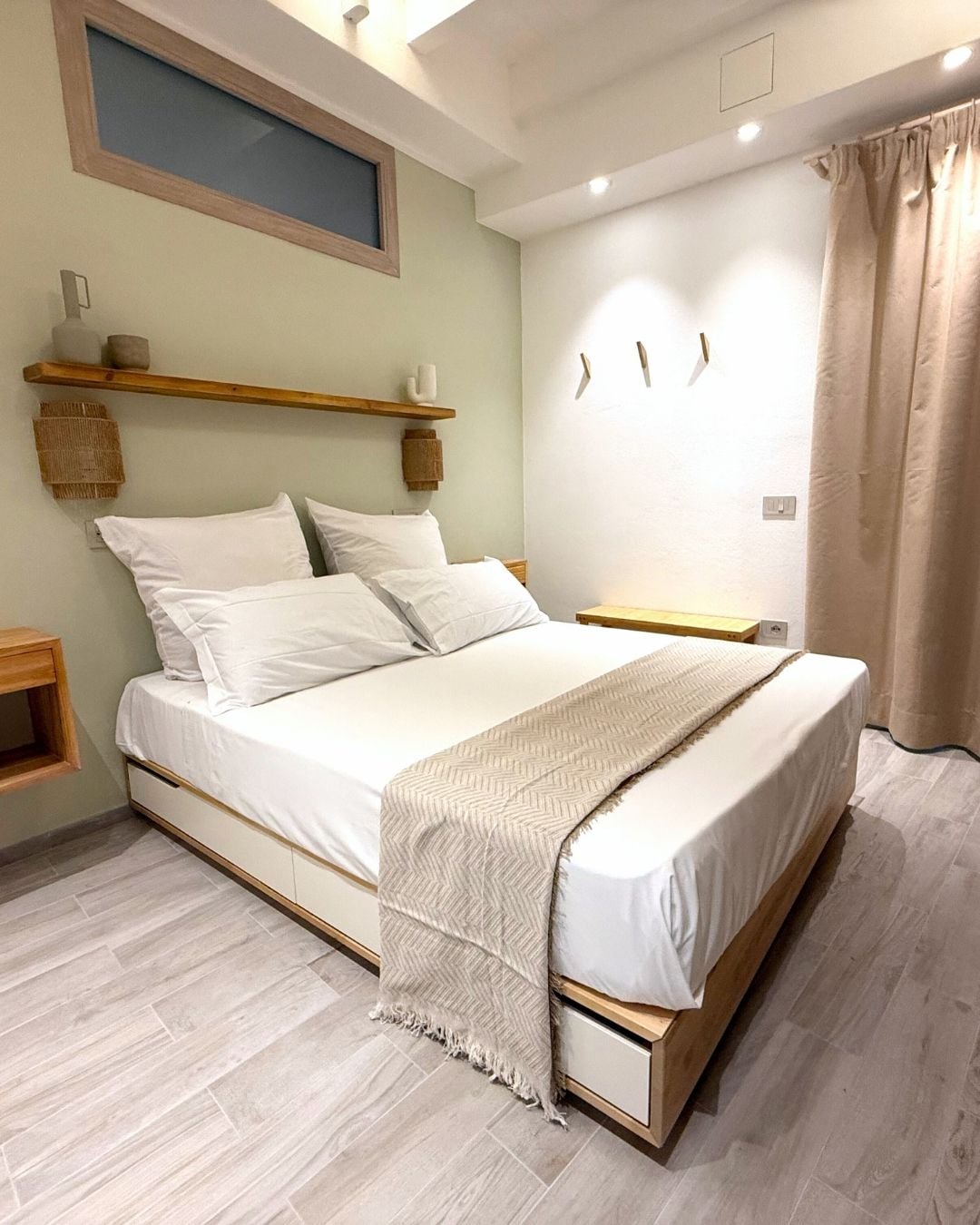 A bedroom with a bed, bedside tables, a headboard, a window, and a wall-mounted light fixture.