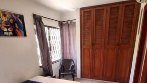 A bedroom with a bed, a chair, a wardrobe, and a painting on the wall. - Gaia Rodadero (Santa Marta)