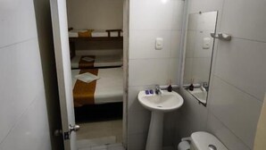 A compact bathroom with a toilet, sink, and mirror. A small bed is visible in the background. - Gaia Rodadero (Santa Marta)