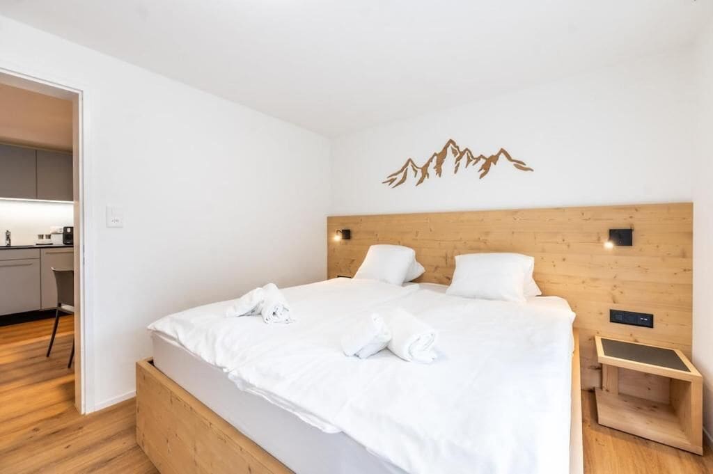 Una camera d'albergo moderna con una testiera in legno, un letto con lenzuola bianche e un piccolo comodino.