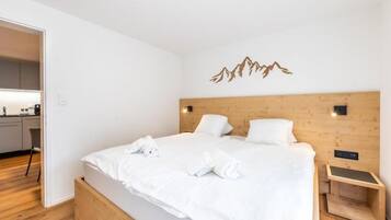 Una camera d'albergo moderna con una testiera in legno, un letto con lenzuola bianche e un piccolo comodino.