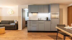 A modern kitchen with grey cabinets, a built-in oven, and a dining area with a table and chairs. - Haus Juliana Trichilti InspiringPlaces Zermatt (Zermatt)