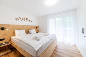 Une chambre à coucher avec une tête de lit en bois, un lit recouvert de draps blancs, une table de chevet et une lampe fixée au mur.
