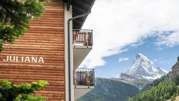 Un edificio chiamato JULIANA, con facciata in legno e balconi, affaccia su un paesaggio montuoso con una cima particolarmente evidente.