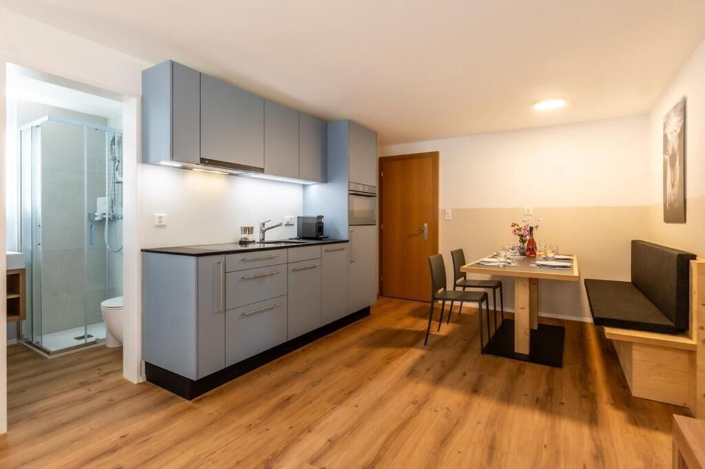 Una cucina compatta con mobili grigi, un'area pranzo con tavolo e sedie, e un pavimento in legno.