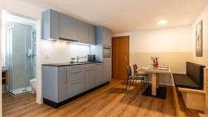 A compact kitchen with grey cabinets, a dining area with a table and chairs, and a wooden floor. - Haus Juliana Trichilti InspiringPlaces Zermatt (Zermatt)