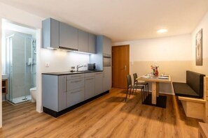 Eine kleine Küche mit grauen Schränken, ein Essbereich mit Tisch und Stühlen sowie ein Holzboden.