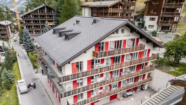 A multi-story hotel with balconies and a ski resort in the background. - Haus Juliana Trichilti InspiringPlaces Zermatt (Zermatt)