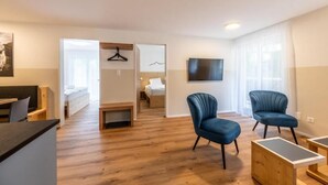 A modern living room with a wooden floor, a flat-screen TV mounted on the wall, and two blue armchairs. - Haus Juliana Trichilti InspiringPlaces Zermatt (Zermatt)