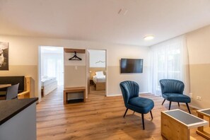 Ein modernes Wohnzimmer mit Holzboden, einem an der Wand montierten Flachbildfernseher und zwei blauen Sesseln.