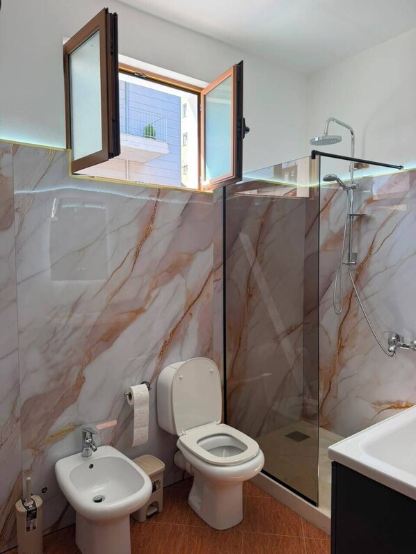 A modern bathroom with a bidet, toilet, and glass-enclosed shower.