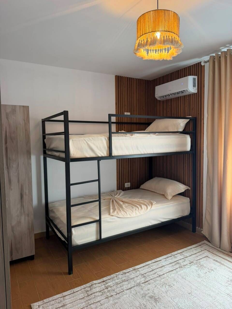 Un lit superposé avec un luminaire au plafond, un appareil de climatisation et une armoire en bois.