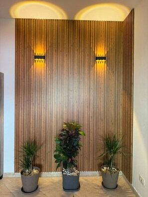 A room with a wooden panel wall, two potted plants, and wall-mounted lighting.
