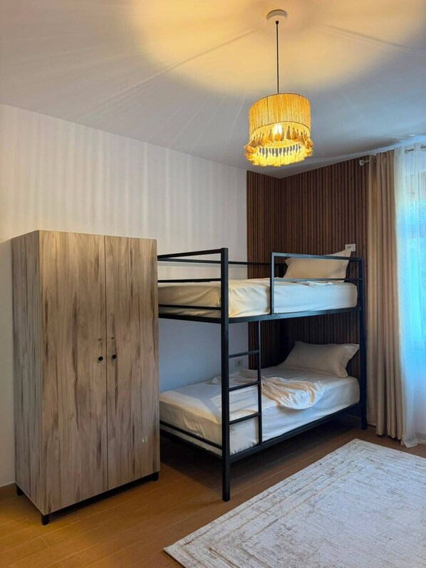 A bunk bed with a wooden wardrobe and a hanging light fixture in a room with a patterned rug.