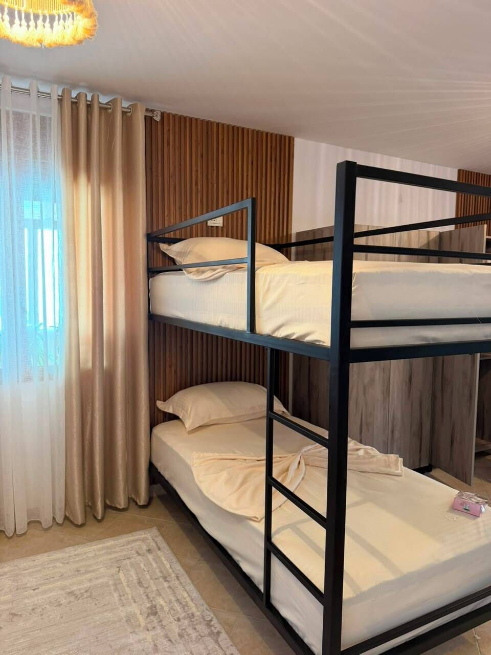 A bunk bed with three levels, a window with curtains, and a wooden wall panel.