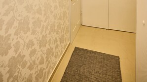 Un couloir avec un papier peint à motifs, un tableau encadré au mur, une porte avec une fenêtre et un tapis sur le sol.