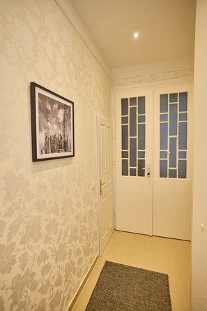 Ein Flur mit gemustertem Wandpapier, einem gerahmten Bild an der Wand, einer Tür mit Fenster und einem Teppich auf dem Boden.