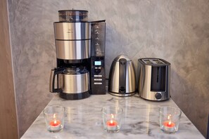 Eine Küche mit Kaffeemaschine, Wasserkocher, Toaster und drei brennenden Kerzen auf der Arbeitsfläche.