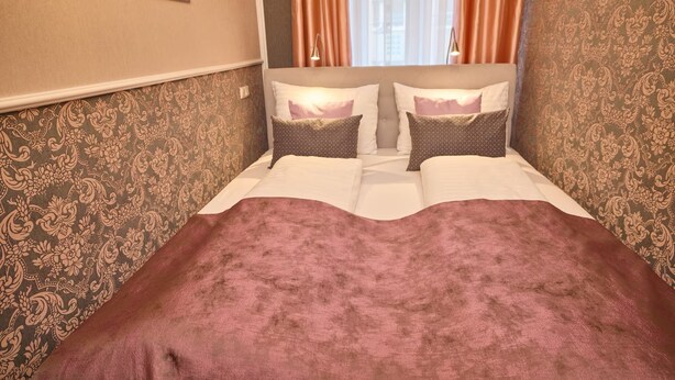 Une chambre d’hôtel avec un lit, deux oreillers, une tête de lit et un papier peint à motifs.